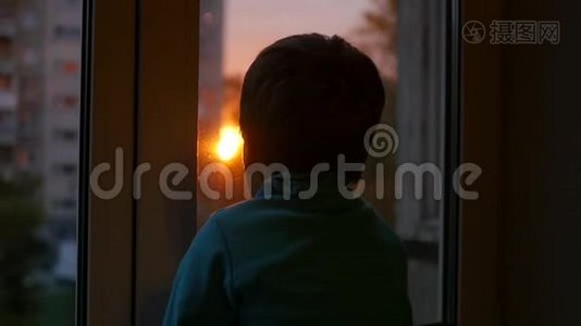 一个孩子站在窗台上，看着窗外的太阳。 日落视频