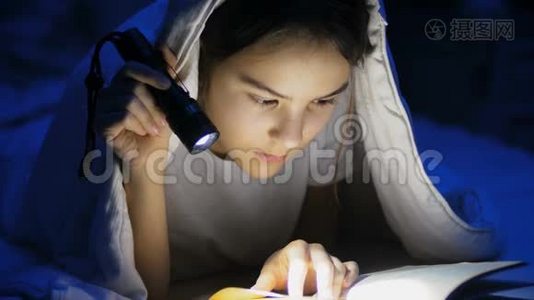 青少年女孩用手电筒在毯子下看书的特写镜头视频