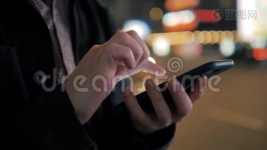 男人在抽象模糊的街头夜晚使用智能手机。 背景夜间城市汽车灯光关闭电话视频