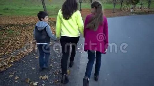 年轻美丽的母亲带着她的孩子在秋天的森林里。 他们在路上跑步很有趣。 他们很开心。 他们视频