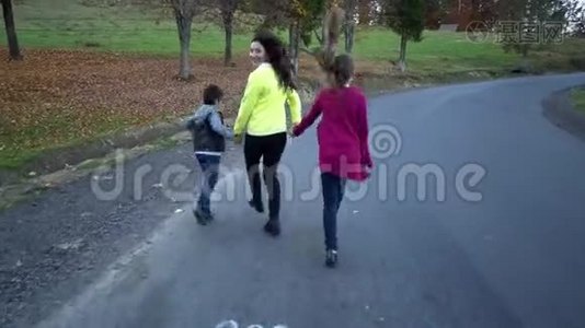 年轻美丽的母亲带着她的孩子在秋天的森林里。 他们在路上跑步很有趣。 他们很开心。 他们视频