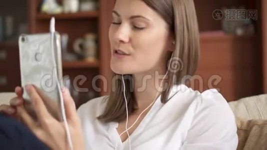 开朗的年轻女性，带着耳机听音乐，唱歌，敲智能手机屏幕视频