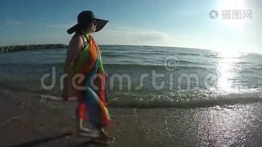 戴帽子的女人在日落时沿着海浪散步视频