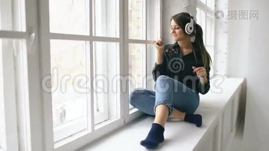带着耳机听音乐跳舞的年轻女子坐在室内的窗户上视频