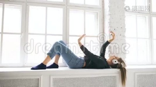 带着耳机听音乐跳舞的年轻女子躺在室内的窗户上视频