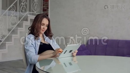 幸福的孕妇坐在玻璃餐桌旁喝咖啡，用平板电脑。 从事商业活动视频