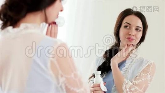 漂亮的年轻女人在镜子前用棉签和保湿乳液做面部护理视频