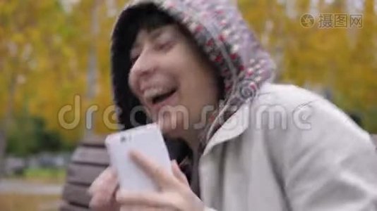 一位身穿连帽衫的年轻女子在秋季公园使用智能手机。视频