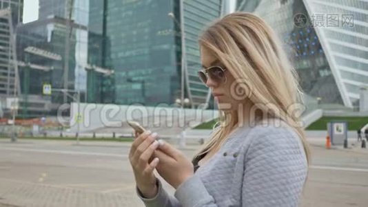 美丽的金发女郎戴着太阳镜，在市中心的背景下使用手机。视频