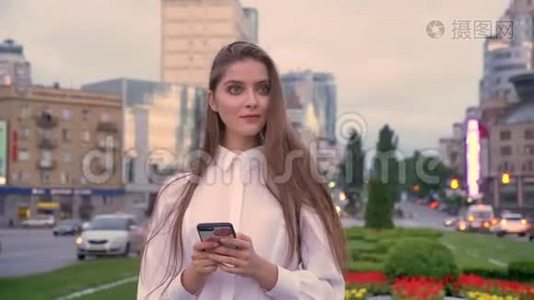年轻漂亮的女孩正在夏季市中心日落时分的智能手机上输入信息，这是一种沟通观念视频