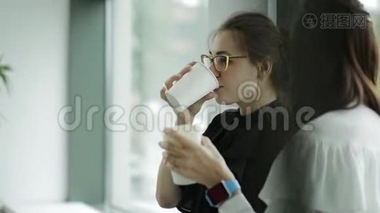 办公室窗口附近的两个女商人在一天结束时喝着咖啡和闲聊视频