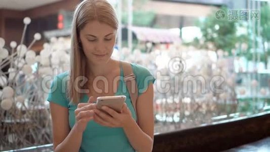 女人坐在购物中心广场上，使用智能手机，浏览看新闻，和朋友聊天视频
