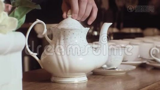 一个人把茶从水壶里倒进木桌上的白色杯子里。视频