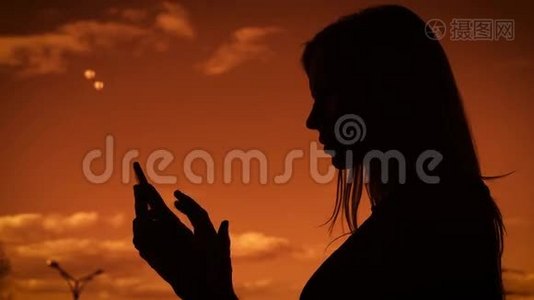 一个成年女孩逆天的剪影，留着长发的女人在手机上打印一条信息。 它用一个小玩意视频