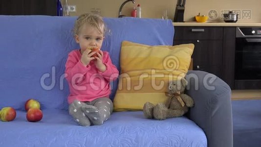 可爱的女婴坐在沙发上吃大苹果水果。视频