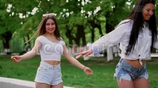 在公园的一个阳光明媚的日子里，两个穿着短短裤的年轻女孩牵着手在赛格威骑车欢笑视频