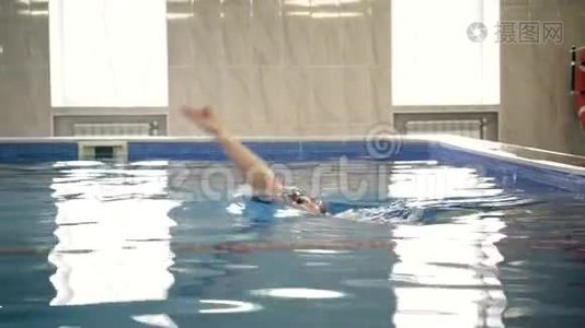 美丽的专业游泳运动员在游泳池里仰泳，镜头拍摄视频
