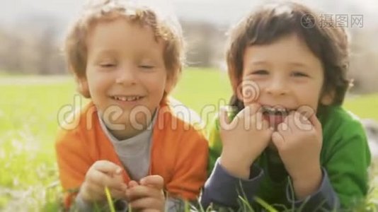 快乐的孩子们微笑着特写肖像。 在草地上躺着的两个哥哥小孩一边笑一边玩视频