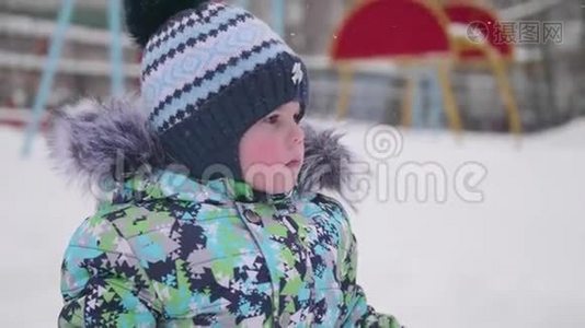 一个小孩在冬天的公园里玩雪.. 孩子拿着铲子，公园里有很多雪。 有趣的游戏视频