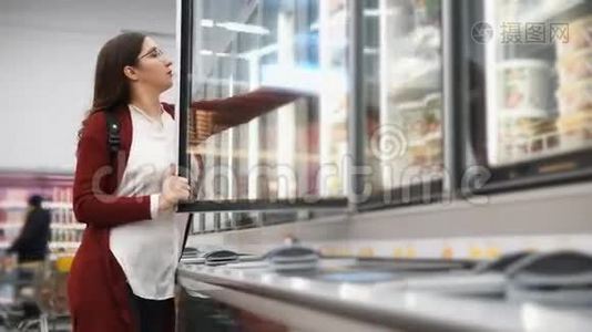 带背包的女人从超市的冰箱里挑选产品。视频