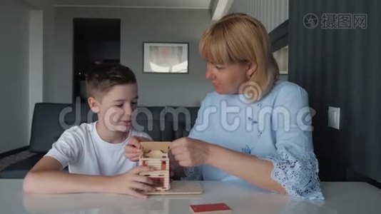 妈妈和儿子坐在一张桌子旁，用木块收集一所房子。 梦想一个私人的家。 游戏和教学视频