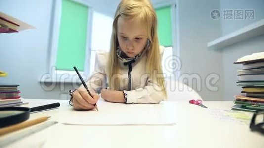 美丽的金发女孩穿着校服坐在桌子旁，用铅笔画画。视频