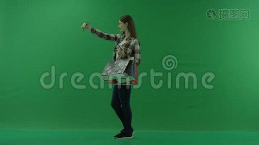 穿着购物袋的女孩站在左边，在绿色屏幕上自拍视频