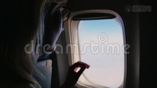 一个年轻的女人关上一扇飞机窗户，看着窗外。 黑暗的框架被照亮的开口视频