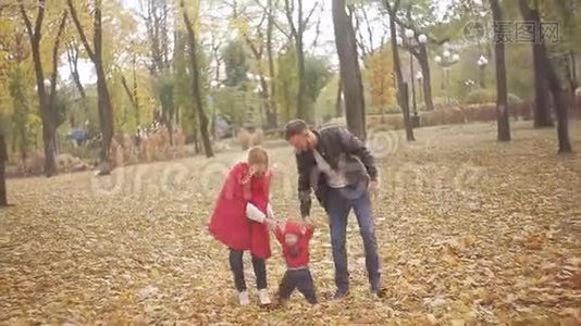 秋天在公园里散步的美丽家庭。 一个小孩学会和他的父母一起走路视频