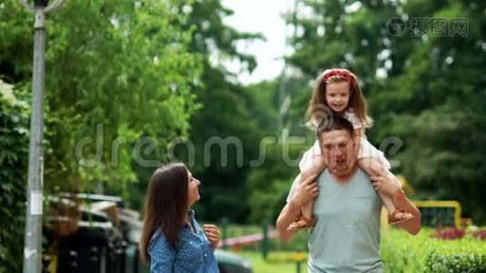 妈妈，爸爸和女儿正沿着街走。 女孩坐在爸爸`肩膀上。 他们笑得很开心。视频