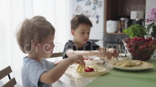 孩子们把草莓卷成薄饼. 孩子们吃煎饼。视频