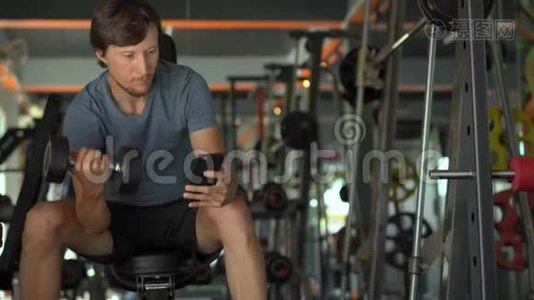 健身房里的一个年轻人在做运动，手里拿着手机在他的眼睛前。 所有的注意力都在视频