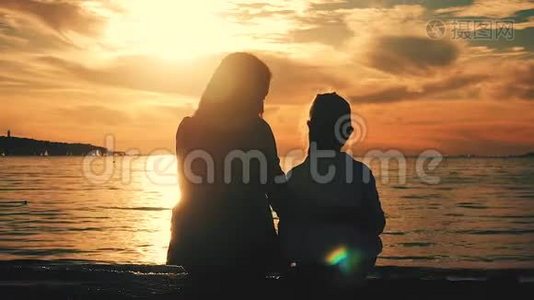 日落时分，母亲和女儿坐在海滩上。 友好家庭观念，生活方式..视频