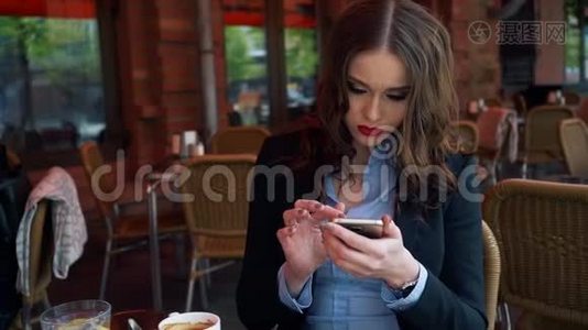 年轻貌美的女士，在餐厅露台上吃早餐时，会看到智能手机屏幕视频