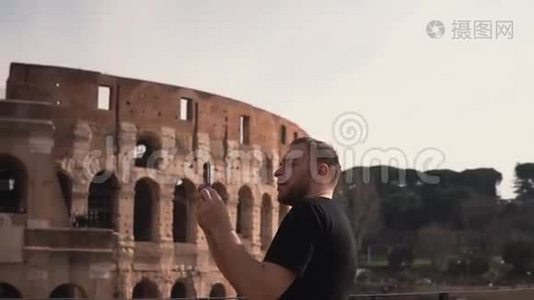 一位英俊的男子访问意大利罗马，在竞技场附近拍照。 他喜欢旅行，建筑。 慢动作。视频