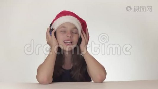 戴着圣诞老人帽子的美丽顽皮的少女在耳机上听音乐，在白色背景上唱歌视频