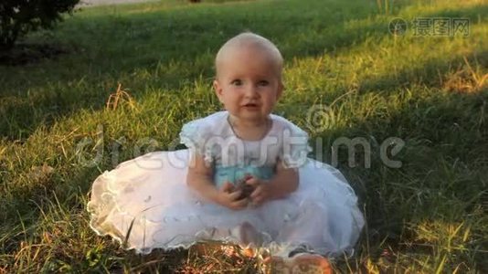 一个小女孩穿着白色连衣裙坐在草地上，拿着一根冷杉。 夏天日落。视频