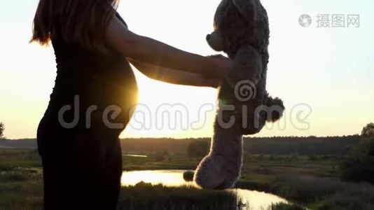 可爱的莫奈-年轻的怀孕女孩在日落时和熊玩。视频