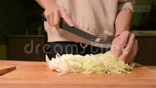 一个女孩在家厨房里用木切割板把皮金斯基卷心菜切成沙拉。 家庭视频