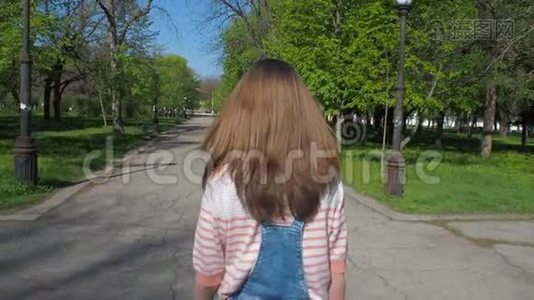 一个戴太阳镜的女孩正在公园里散步。 这个女孩是个穿着牛仔裤混搭的少年。 女孩的情绪。 慢动作。视频