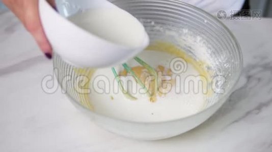 近距离观看女性手倒牛奶到碗准备面团和混合配料使用搅拌器。 自制视频
