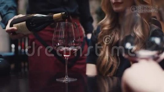 一个服务员把红酒倒在杯子里，为一个有着优雅发型的迷人的年轻女人。 玩得开心视频