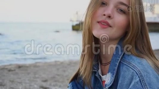 慢动作特写的可爱女孩谁微笑和看相机，坐在海滩上温暖的夏天晚上。视频