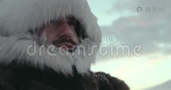 一幅穿着传统驯鹿外套的站立男子在寒冷的冬天蒸汽和看着特写。 北极考察视频