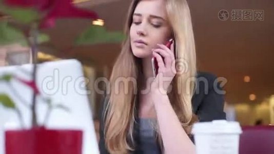 可爱的女孩坐在咖啡馆里。 她正在用她的智能手机和笔记本工作。视频
