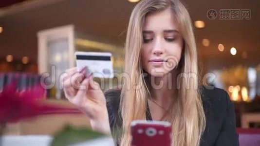 穿黑色夹克的可爱女孩在咖啡馆A©。 她在智能手机上的银行卡数据方面处于领先地位。视频