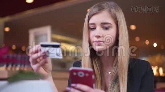 穿黑色夹克的金发美女在咖啡馆A©。 她在智能手机上的银行卡数据方面处于领先地位。视频