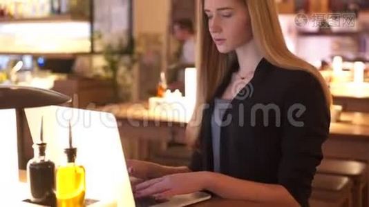那个穿着黑色夹克的金发女郎坐在咖啡馆A©里。 她专注于和她一起工作视频