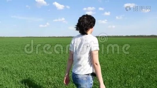 穿着牛仔裤走在绿色草坪上的年轻女子，动作缓慢。 女孩正走在草坪上视频