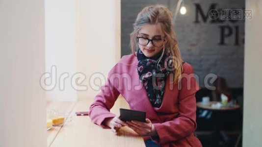 可爱的小女孩穿着休闲装，坐在咖啡馆里，用她的平板电脑上网，看着©。视频